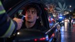 Un giovane al volante sottoposto all'alcoltest durante un controllo notturno, con le luci della polizia sullo sfondo