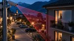 Telecamera su un palo in un borgo al crepuscolo, con il cono di ripresa che raggiunge il balcone e la finestra illuminata di una abitazione privata